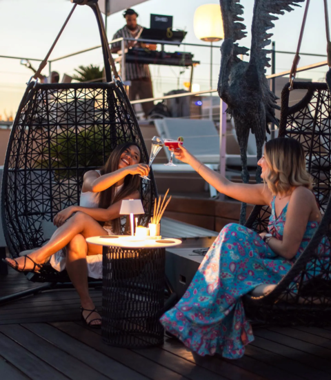 Joyful moment captured on the rooftop of Hotel de Paris Saint Tropez with two smiling girls cheering between DJs playing vibrant music photo by Marc de Delley